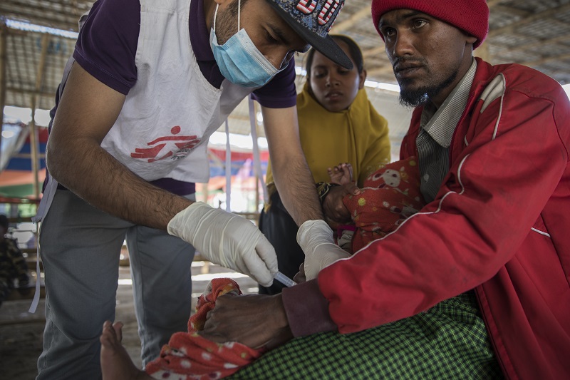 Rohingya refugee Boshir Ullah, 25, helps MSF staff vaccinate his youngest child Ferungada at Sabrang entry point. Photo: Anna Surinyach/MSF