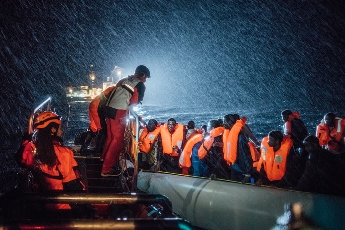 Rescuers from SOS Mediterranee, with whom MSF partners on board the search and rescue ship Aquarius, distribute lifejackets in heavy seas and pouring rain to refugees adrift on a small inflatable boat in the Mediterranean Sea.