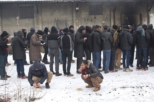 People eat a meal as others queue in a food line at an abandoned warehouse used by refugees as shelter in Belgrade, Serbia