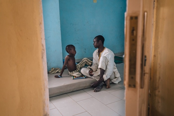 Zahardien Musa, a 14-year-old meningitis patient from Sokoto, rests on his bed with his father at the Muhammed Murtala Specialist Hospital.