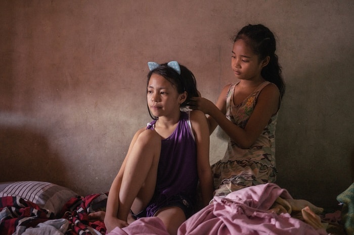 Elyes (L) and Diana fix each other's hair before posing for a portrait in their tenement home near Smokey Mountain, Manila. Both girls have received vaccinations from the Likhaan clinic, which provides free healthcare for low income communities. For many members of low income communities in Manila, procuring basics such as food, shelter, and clothing takes priority over their healthcare needs.