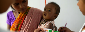 A mother looks on as her child is measured with a MUAC tape for symptoms of malnutrition at Pusalota health centre.