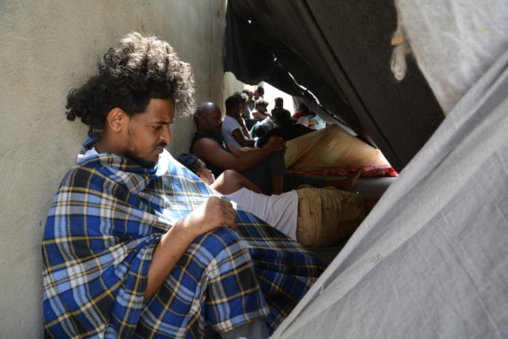 Refugees outside try to protect themselves from the sun by leaning back on the walls of the buildings in Zintan detention centre. Libya, June 2019.
©JÉRÔME TUBIANA/MSF