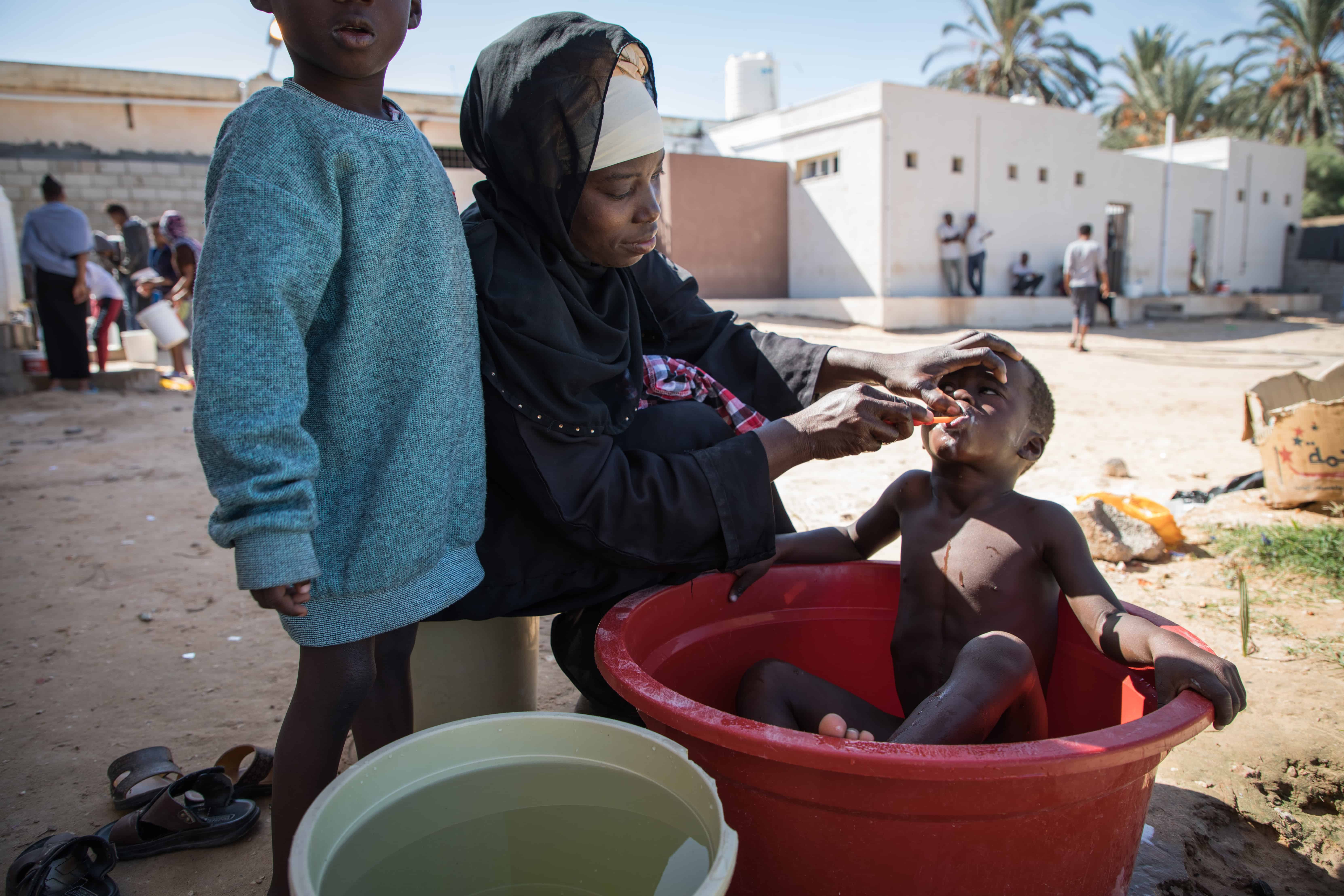 A mother brushes her child's teeth while giving him a bath within the confines of the Souq Al-Khamis detention centre. Khoms, Libya, October 2019.
© AURELIE BAUMEL/MSF