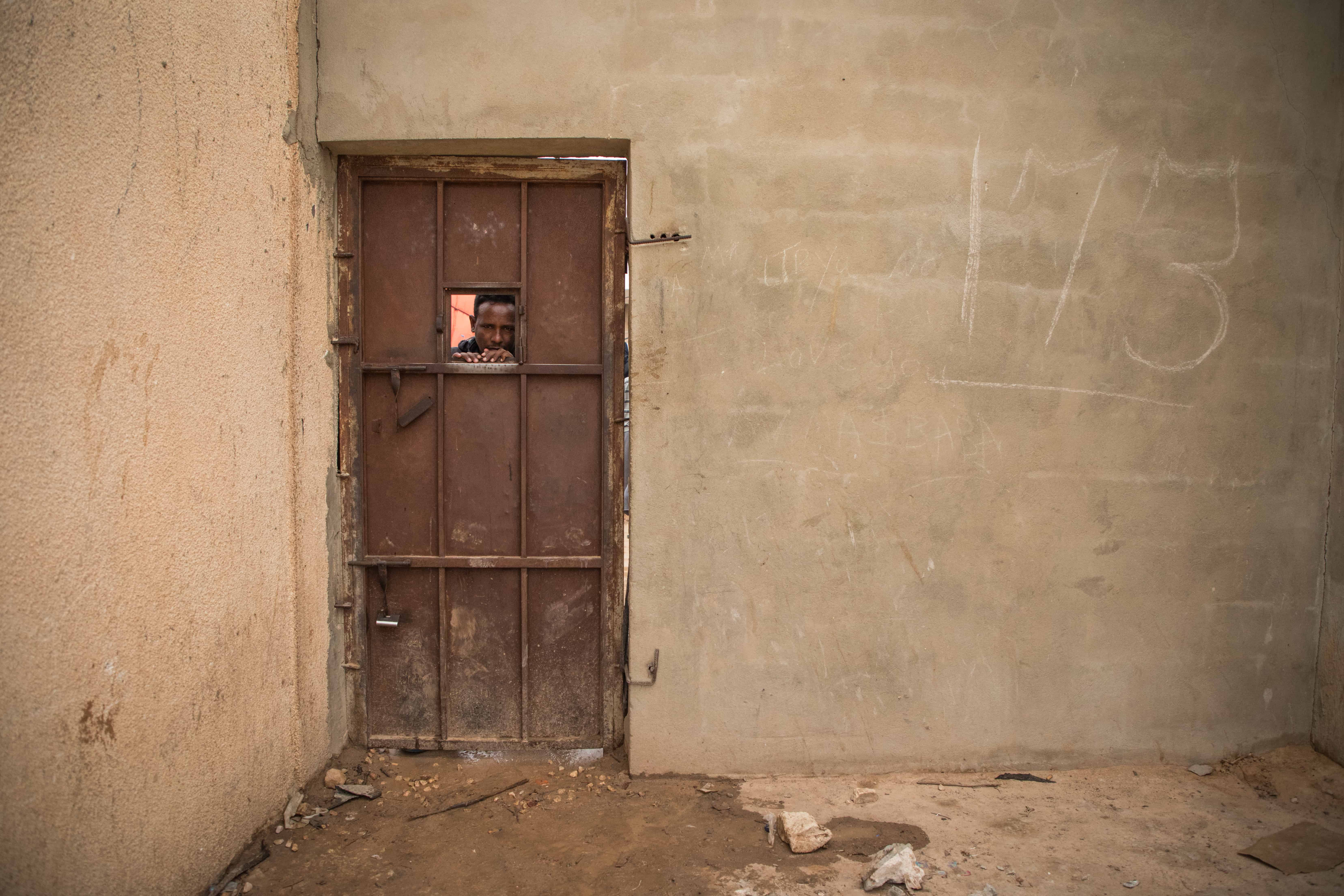 A man peers out through a gap in the gate of the Dahr-El-Jebel detention centre. Libya, October 2019. © AURELIE BAUMEL/MSF