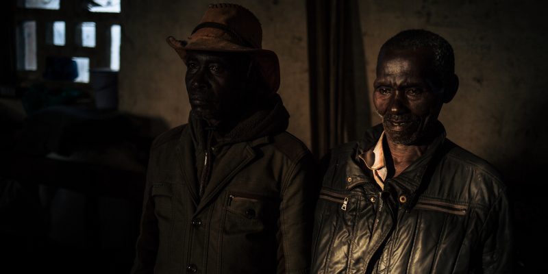 Two men stand in a hall in Drodro parish, which hosts more than 14,000 people who have fled armed attacks in their village, DRC, November 2019. © ALEXIS HUGUET