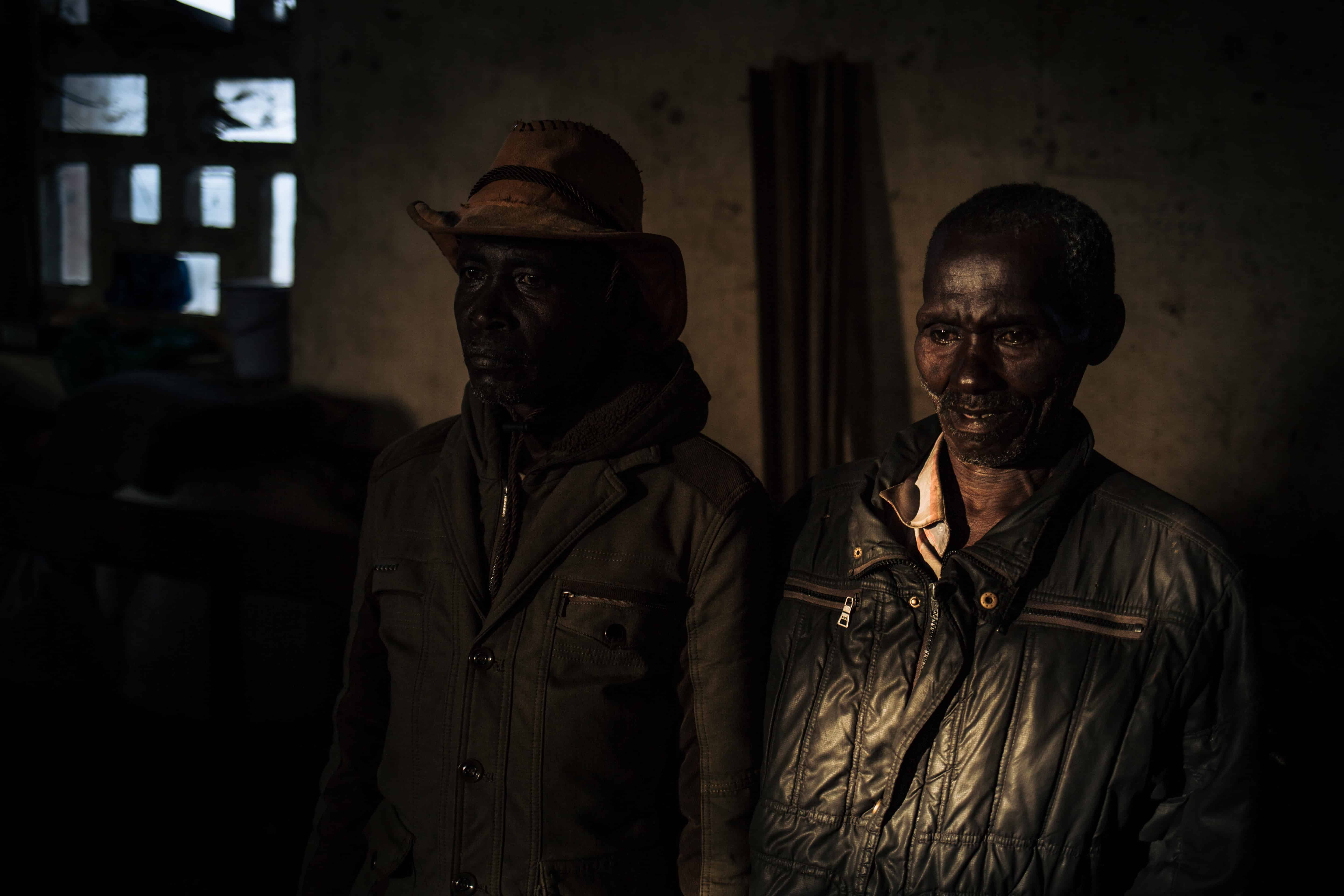 Two men stand in a hall in Drodro parish, which hosts more than 14,000 people who have fled armed attacks in their village, DRC, November 2019. © ALEXIS HUGUET