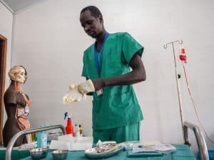 Gabriel Kalany, MSF Academy student in Old Fangak, gets ready for a session of practice at the Skills Lab. After arranging his trolley with all required tools to perform the placement of a urinary catheter on a mannequin, he puts on disposal gloves. After 18 months of training, Gabriel graduated from the MSF Academy in Old Fangak in June 2022.