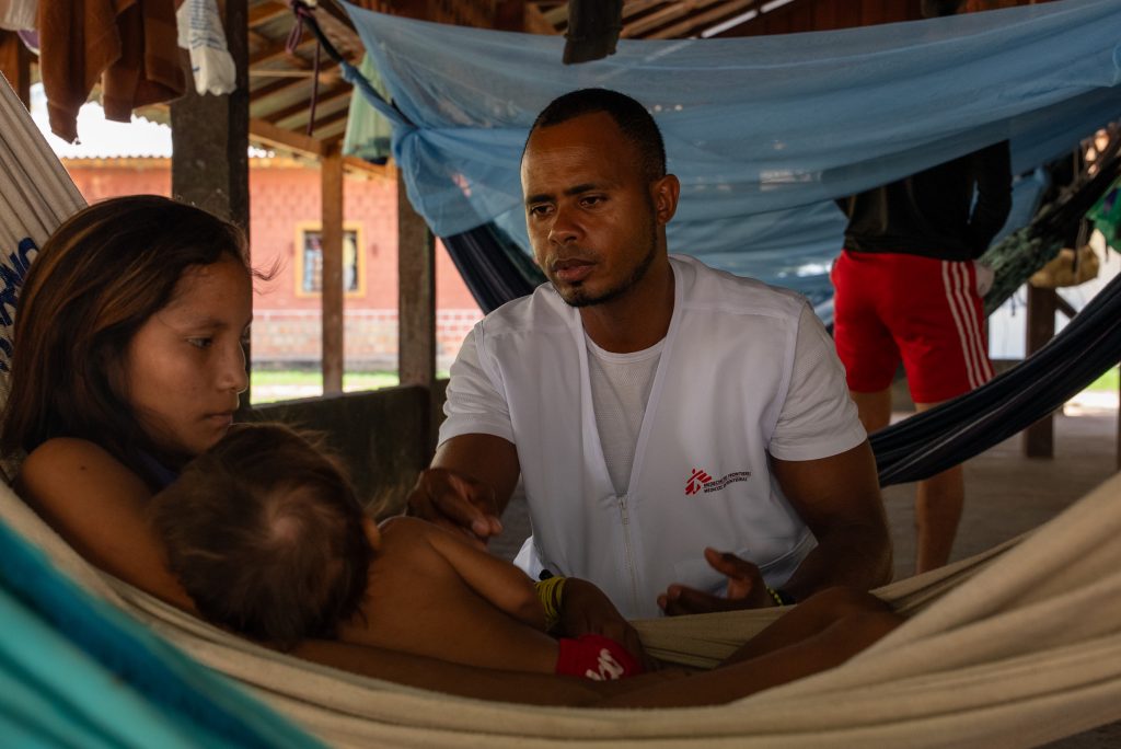 Reydanner Blez, an MSF health promoter, conducts a health follow-up visit in a maloca (large comunal dwelling). Through these visits, the health promotion team monitors malaria treatment and assesses the health status of inpatients and their families. This ongoing support helps ensure adherence to treatment protocols, contributing to safer care and facilitating patient discharge. ©️Marília Gurgel/MSF