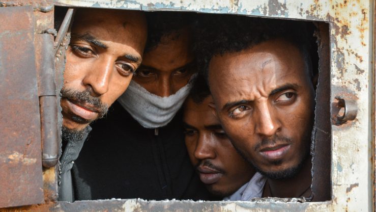 Refugees in Zintan DC at the gate of the main warehouse where 700 of them were detained. A tuberculosis outbreak has likely been raging for several months in the detention centre and some wear masks for fear of contamination. The main warehouse was emptied in June 2019, and the remaining people distributed among the other buildings within the detention centre compound.